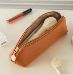 Brown makeup pouch with brushes and a lip product on a light surface