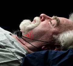 Close-up of a person wearing a black anti-snoring device, against a dark background.