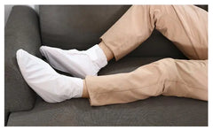 Person wearing white mask sleeve and beige pants sitting on a gray couch.