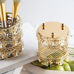 Decorative gold and crystal container with makeup brushes on a white surface.
