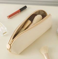 Beige makeup pouch with brushes and a lip gloss on a light surface