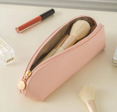 Pink makeup pouch with brushes and lip gloss on a light surface