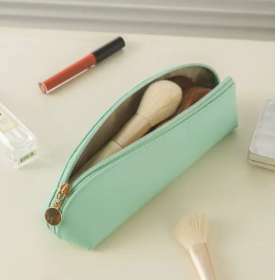 Mint green makeup pouch with brushes and a lip gloss on a light surface