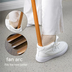 Person wearing white sneakers with a close-up of a shoehorn in the back of a shoe on a concrete floor.